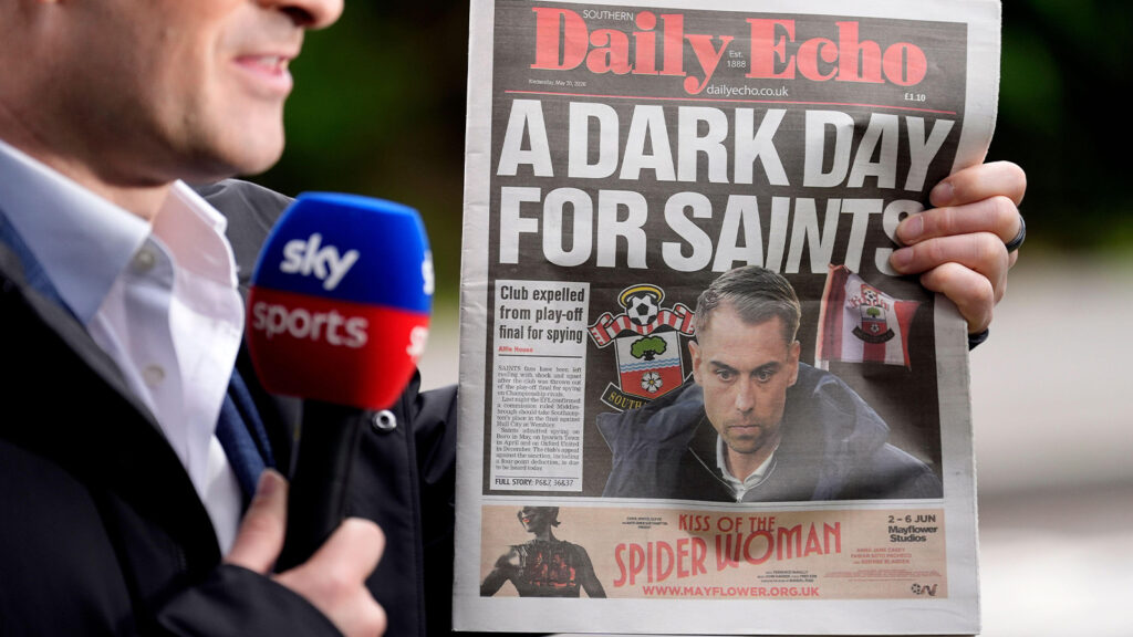 Ett exemplar av Southern Daily Echo, med Southamptons tränare Tonda Eckert på omslaget, hålls upp under en direktsändning i Sky Sports utanför Staplewood Campus, Southampton FCs träningsanläggning. Southampton har uteslutits från Championship-slutspelet efter att ha erkänt att klubben spionerat på motståndare vid tre tillfällen den här säsongen, däribland på slutspelsmotståndaren Middlesbrough FC tidigare denna månad. Klubben har också fått fyra poängs avdrag inför nästa säsong, samtidigt som Middlesbrough återinsatts i slutspelet och väntas ta Southamptons plats i lördagens final mot Hull City. Bilddatum: onsdagen den 20 maj.
